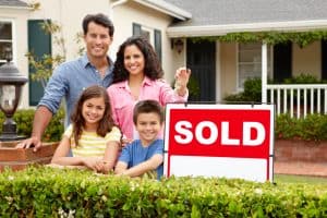 Family with sold sign in front of house